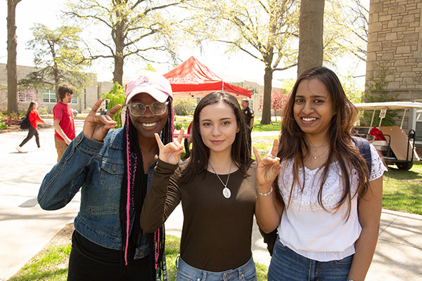 Three students posing with the "snouts out" hand signal.