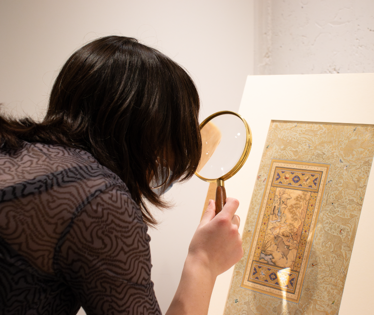 Image of student looking through magnifying glass at a piece of art.