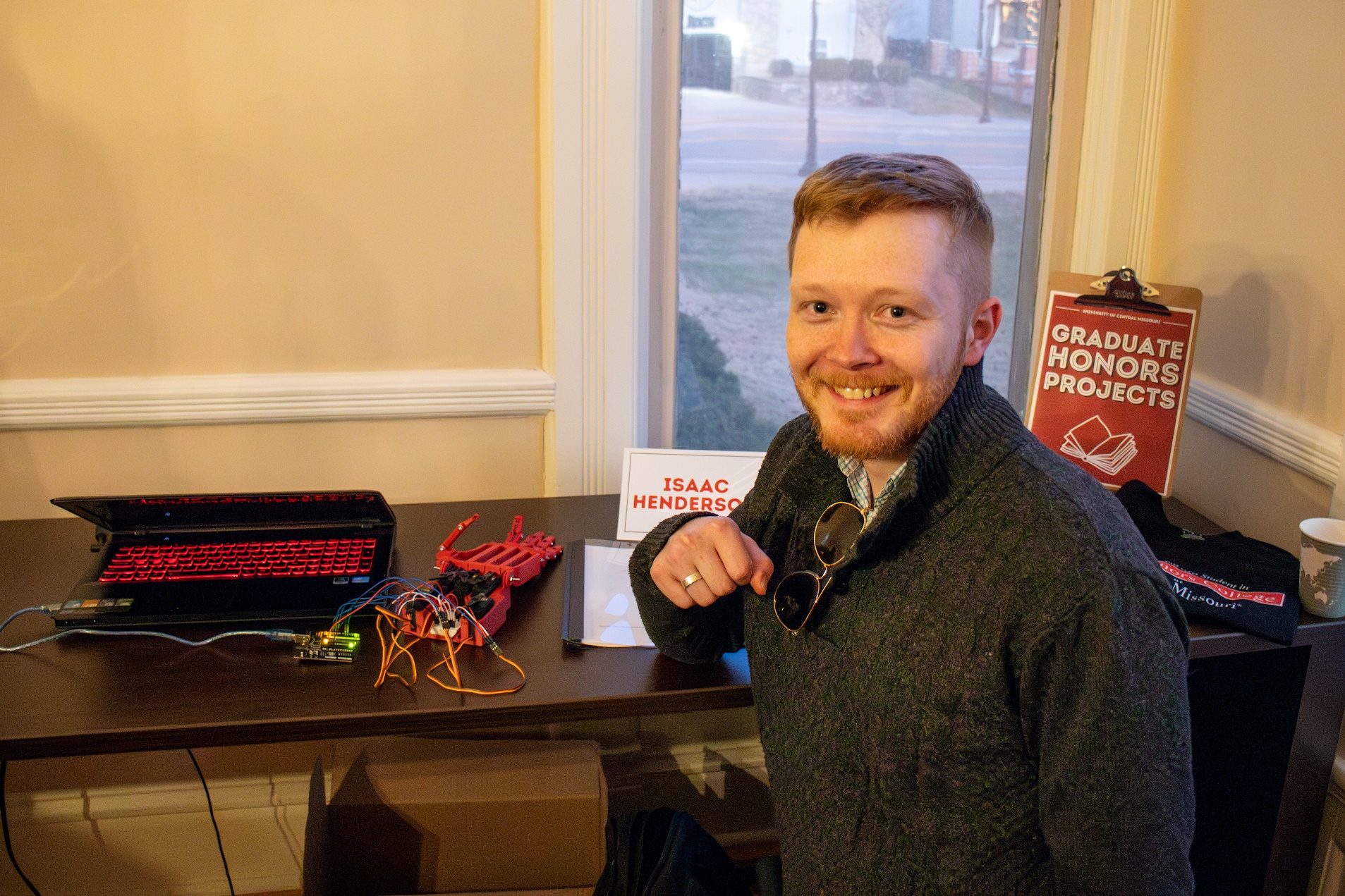 Honors student posing next to their Honors Project. Honors student posing next to robotic hand.